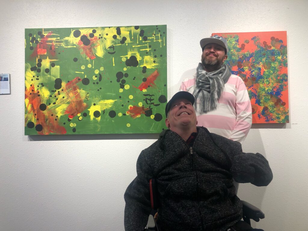 Visual Artist Corey and his tracker, Louis Trujillo stand in front of Corey's painting.