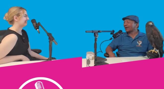 Emma and Kin smile in front of microphones on a blue background
