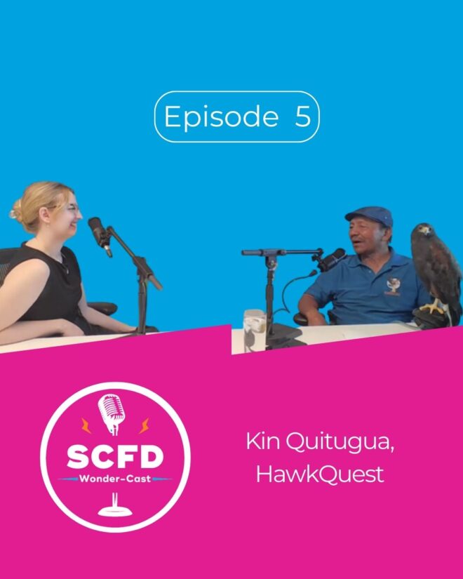 Emma and Kin smile in front of microphones on a blue background